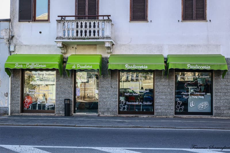 immagine esterna del negozio, ovvero quattro vetrine, con tende esterne di colore verde chiaro